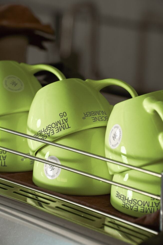 Row of lime ceramic mugs with circular brand logo labels on shelf
