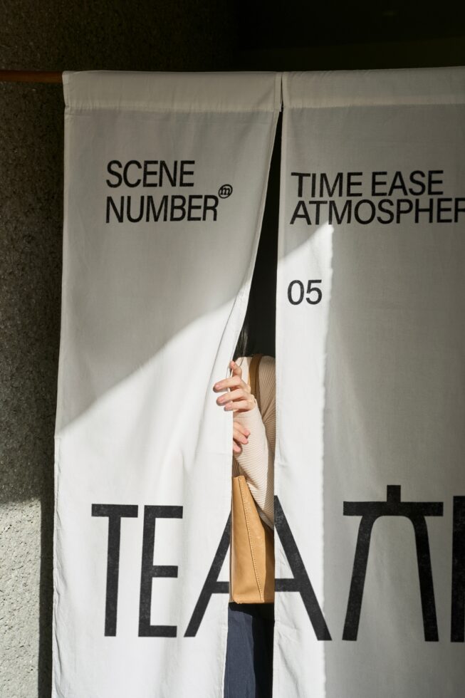 Split view of white door curtain panels with black text, person peeking through center gap