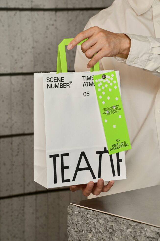 Person holding white paper bag with lime green handles, Scene Number branding visible