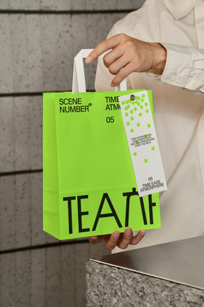 Hands holding large neon tote with branding tag against industrial gray background