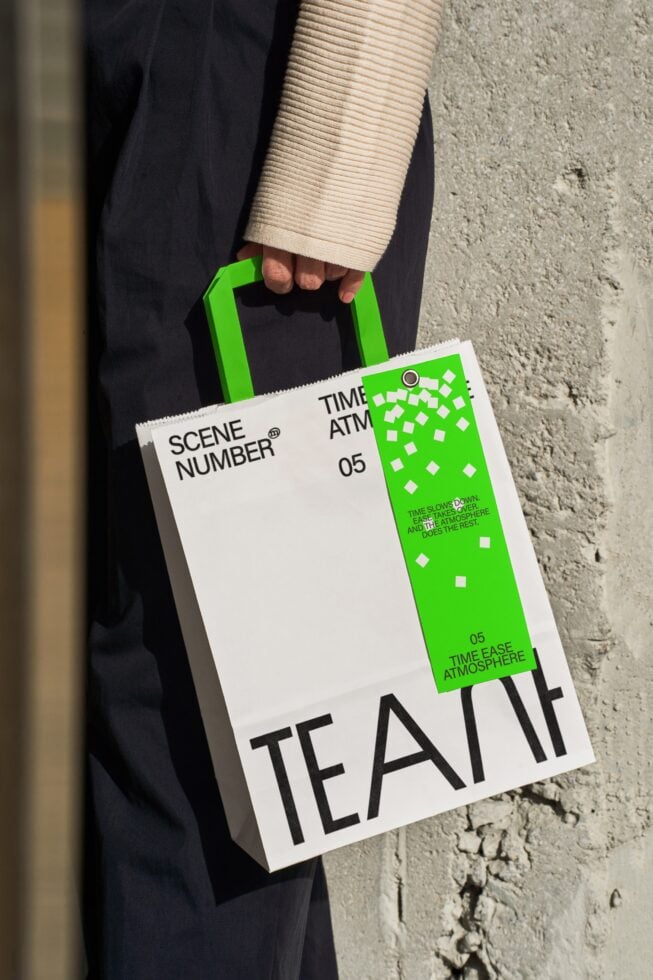 Person carrying white paper bag with green branding element in urban street setting