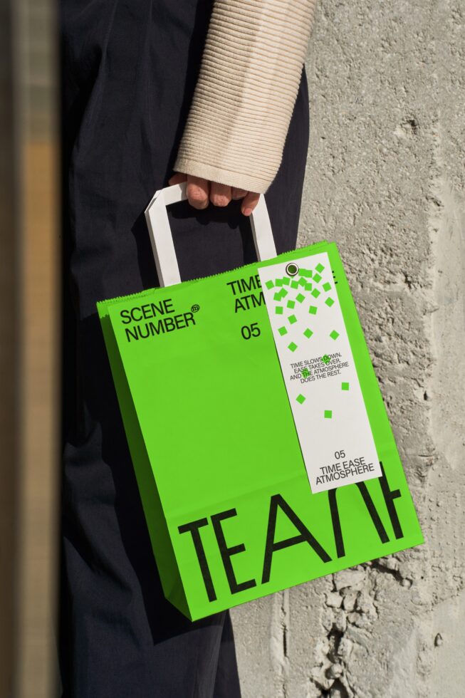 Person in beige cardigan holding bright green tote bag with white tag on concrete wall