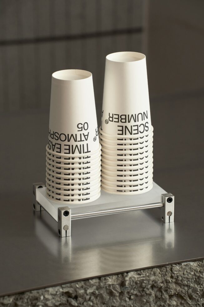 Two white paper cups displayed on metal bracket fixture in neutral environment