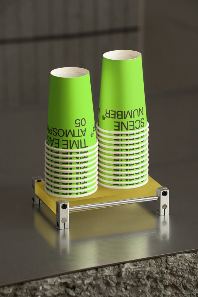 Two green paper cups on yellow stand with metallic brackets in studio