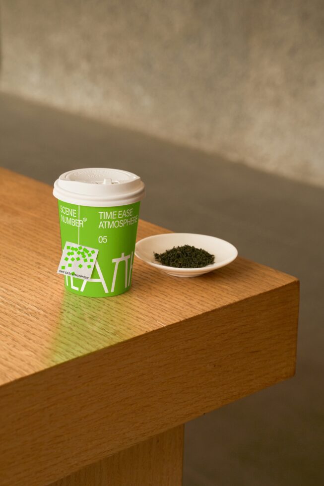Green canister with white cap on wooden block next to loose tea leaves