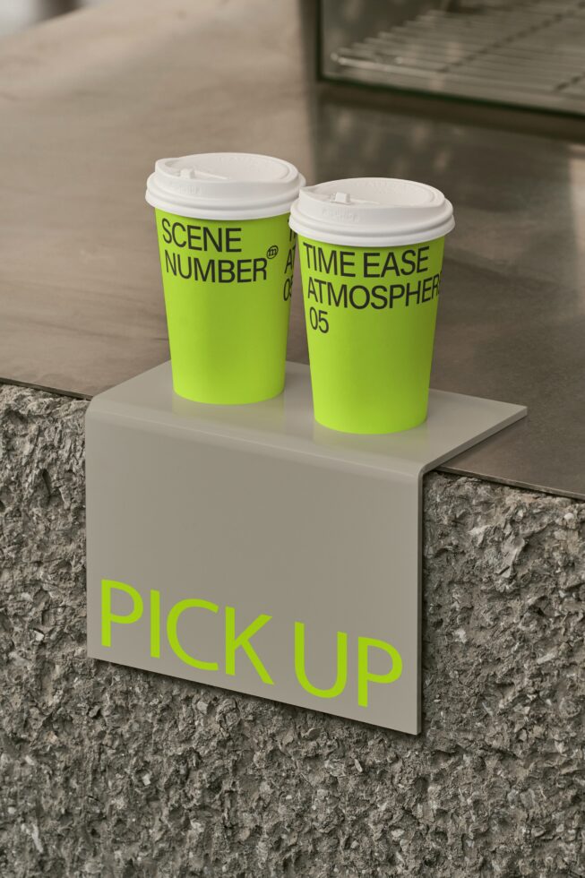 Two neon yellow coffee cups with Scene Number branding on white pedestal