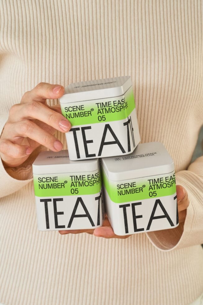 Hands holding three stacked green tea packaging boxes with white labels