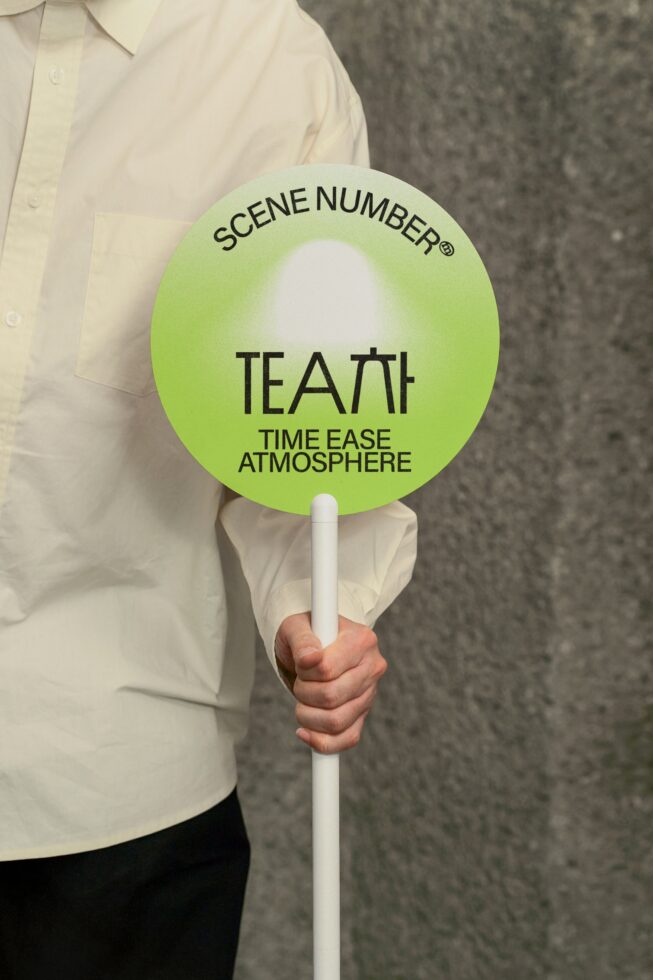 Person holding round green scene number clapper board with white handle