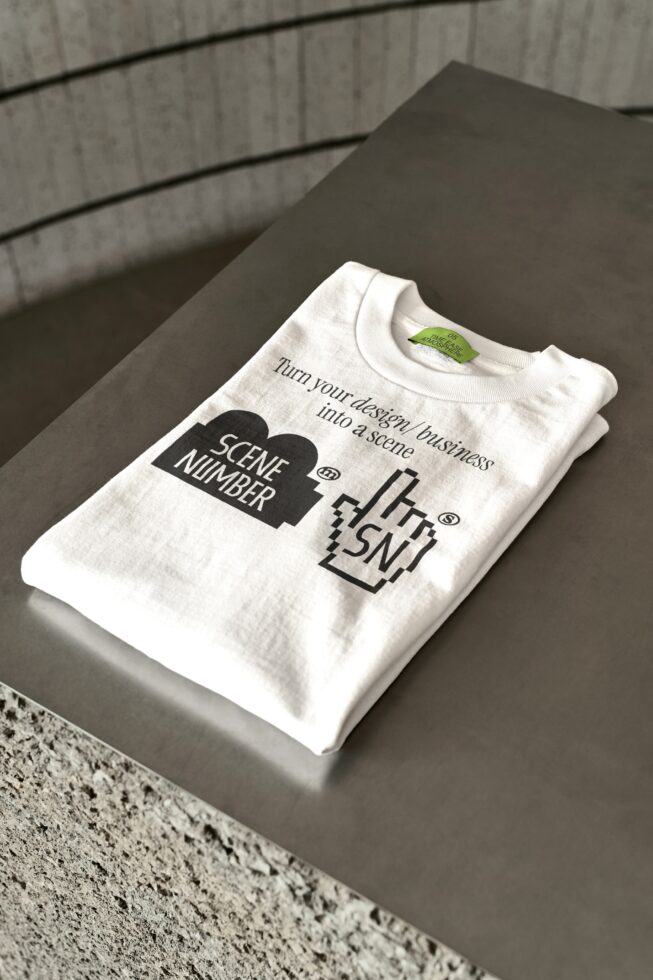 Folded cream tee on concrete surface showing Scene Number logo with tea service tagline printed on chest