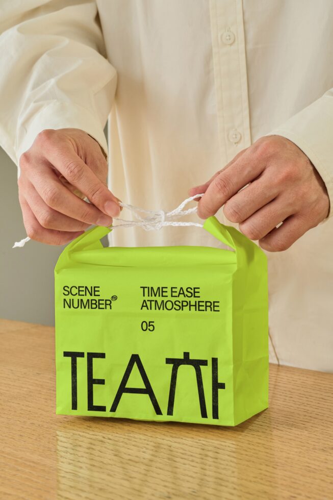 Hands holding open lime green tea box with twisted twine handles showing Scene Number branding inside