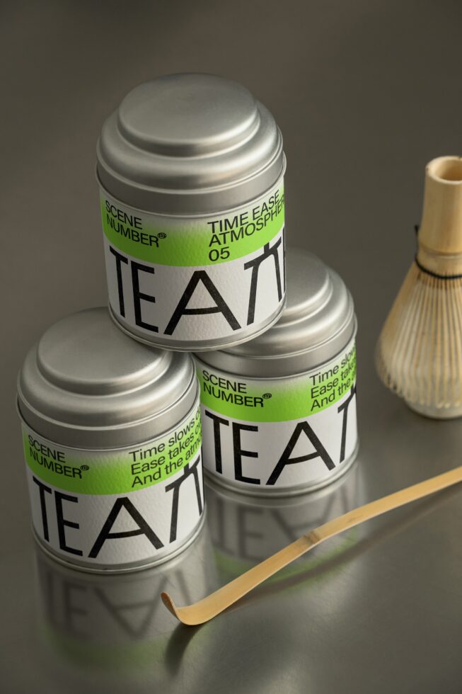 Three stacked metallic tea canisters with bright green labels, wooden accessories nearby