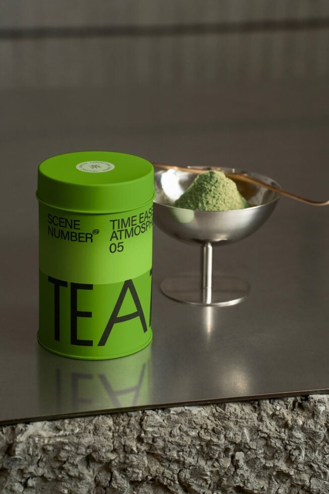 Bright green cylindrical tea tin next to steel bowl with matcha powder