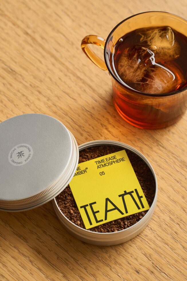 Loose tea in open container with cream lid, glass of iced tea on wooden surface