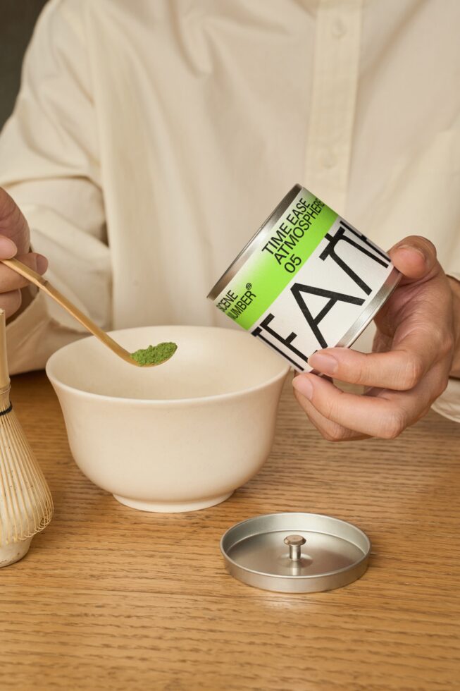 Hand holding lime tea box next to ceramic bowl with matcha preparation tools