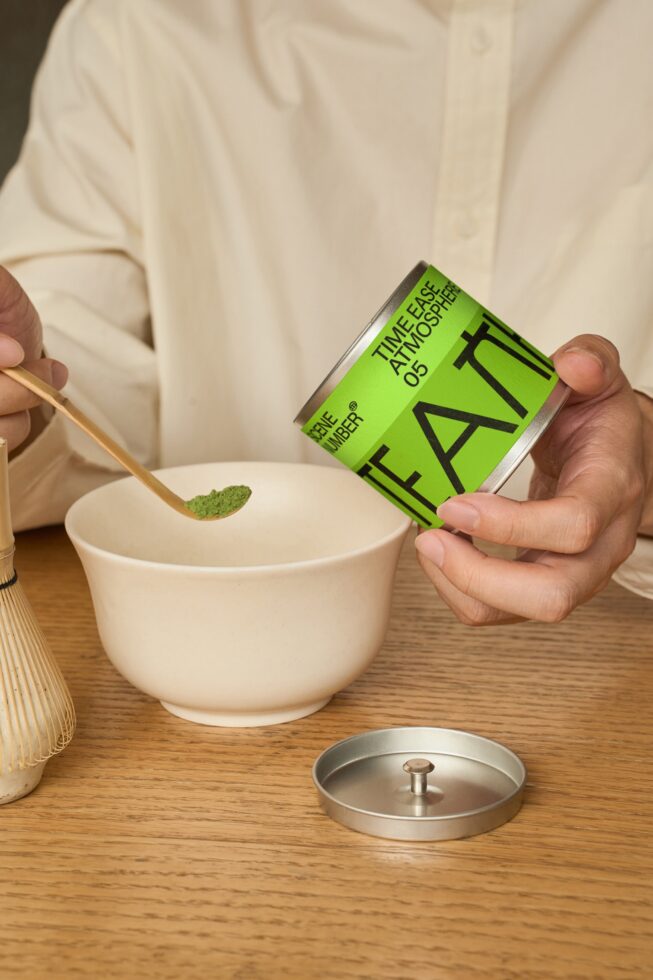 Person pouring from lime green tea box into ceramic bowl with matcha whisk