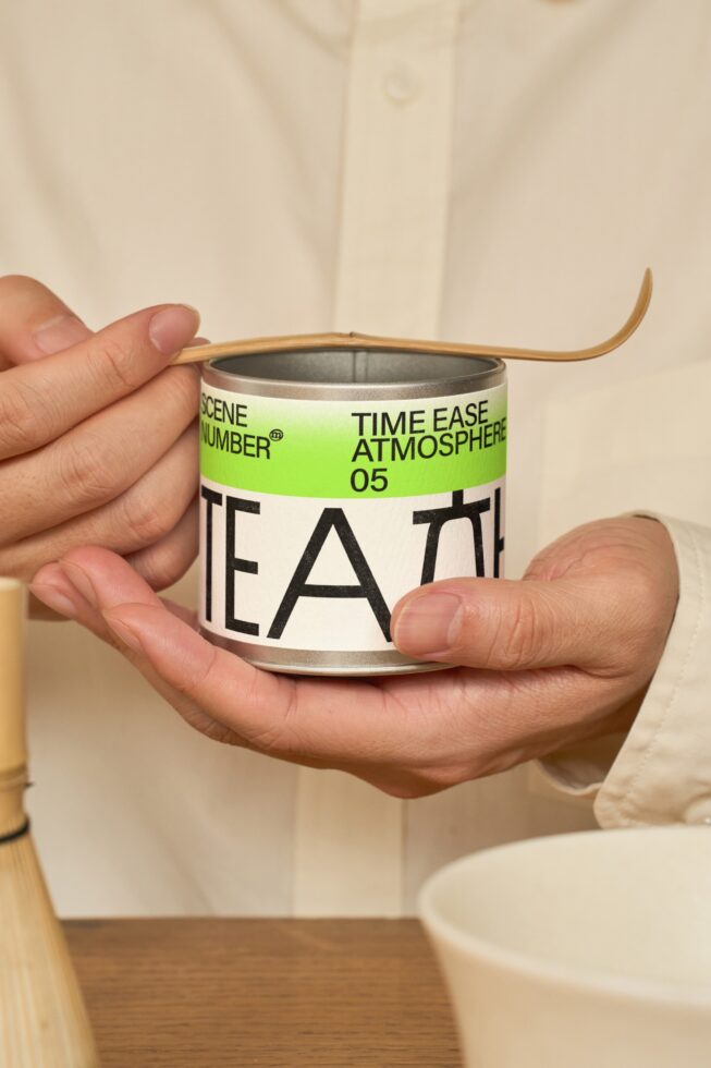 Person holding white tea container with green label, wooden accessory detail
