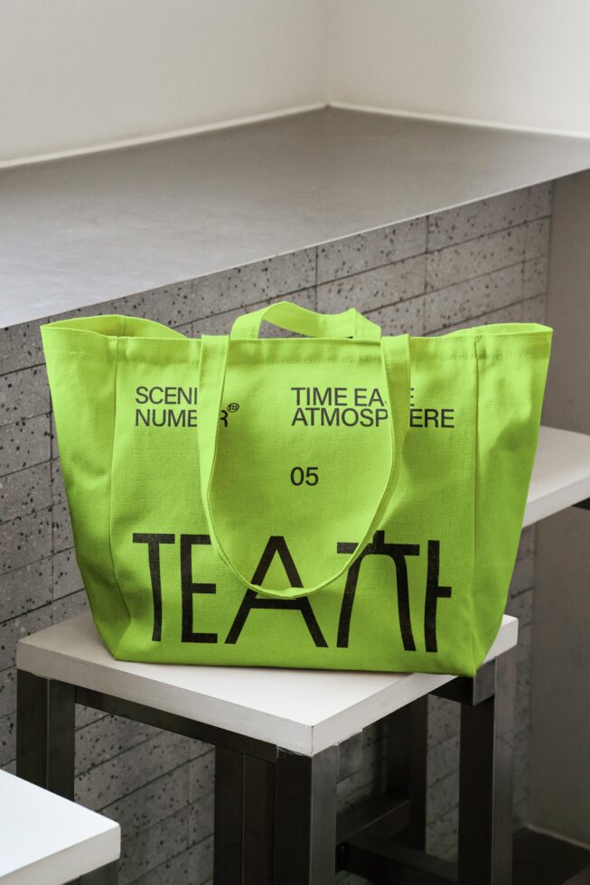Lime colored tote bag on white shelf against concrete textured backdrop
