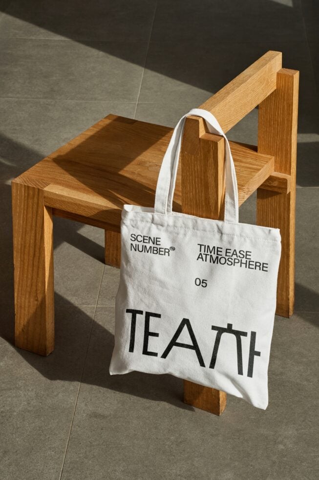 White canvas tote bag draped over wooden chair with black tea branding