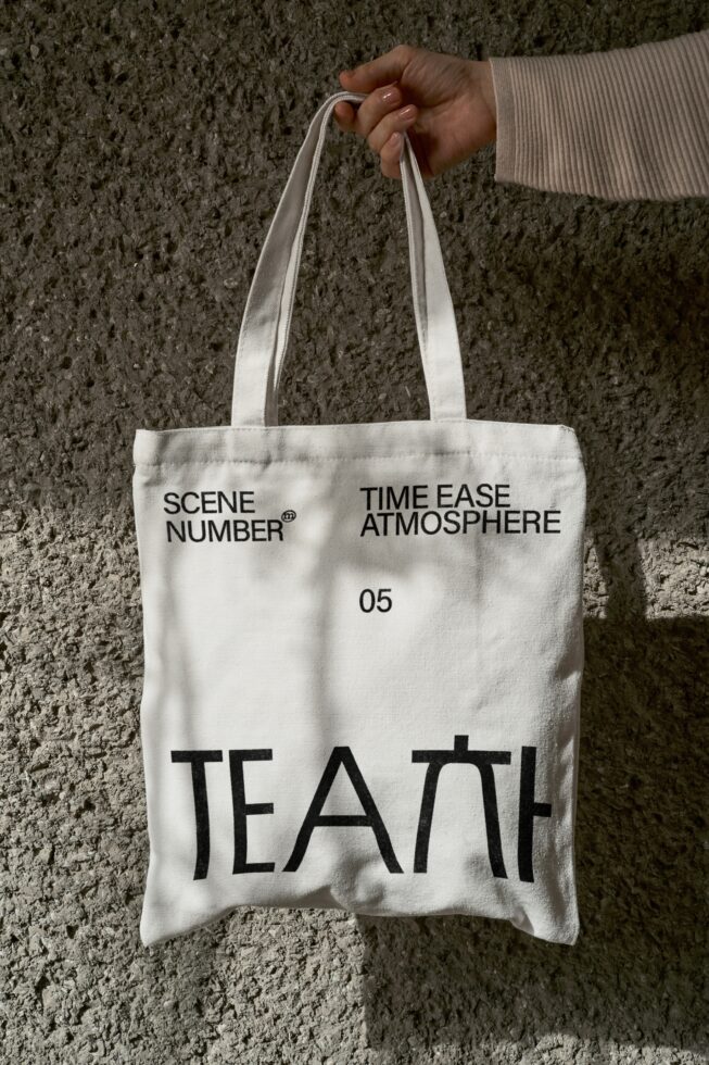 Cream canvas tote bag held up against concrete wall showing printed text