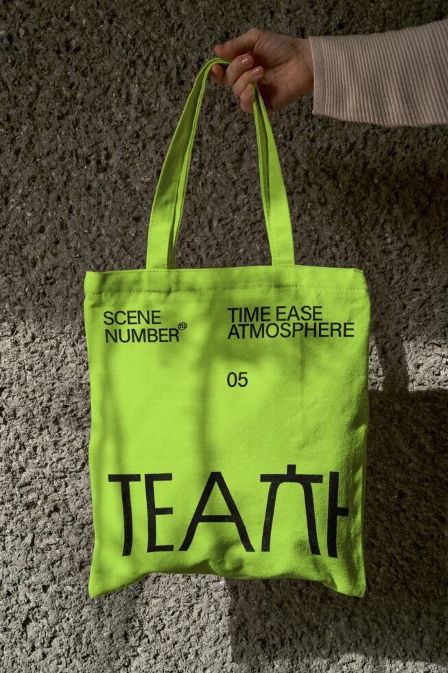 Neon lime tote bag held against textured concrete wall backdrop
