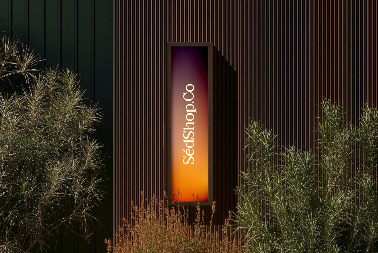 Tall narrow display with warm gradient lighting, dry plants framing vertical sign on ribbed wall