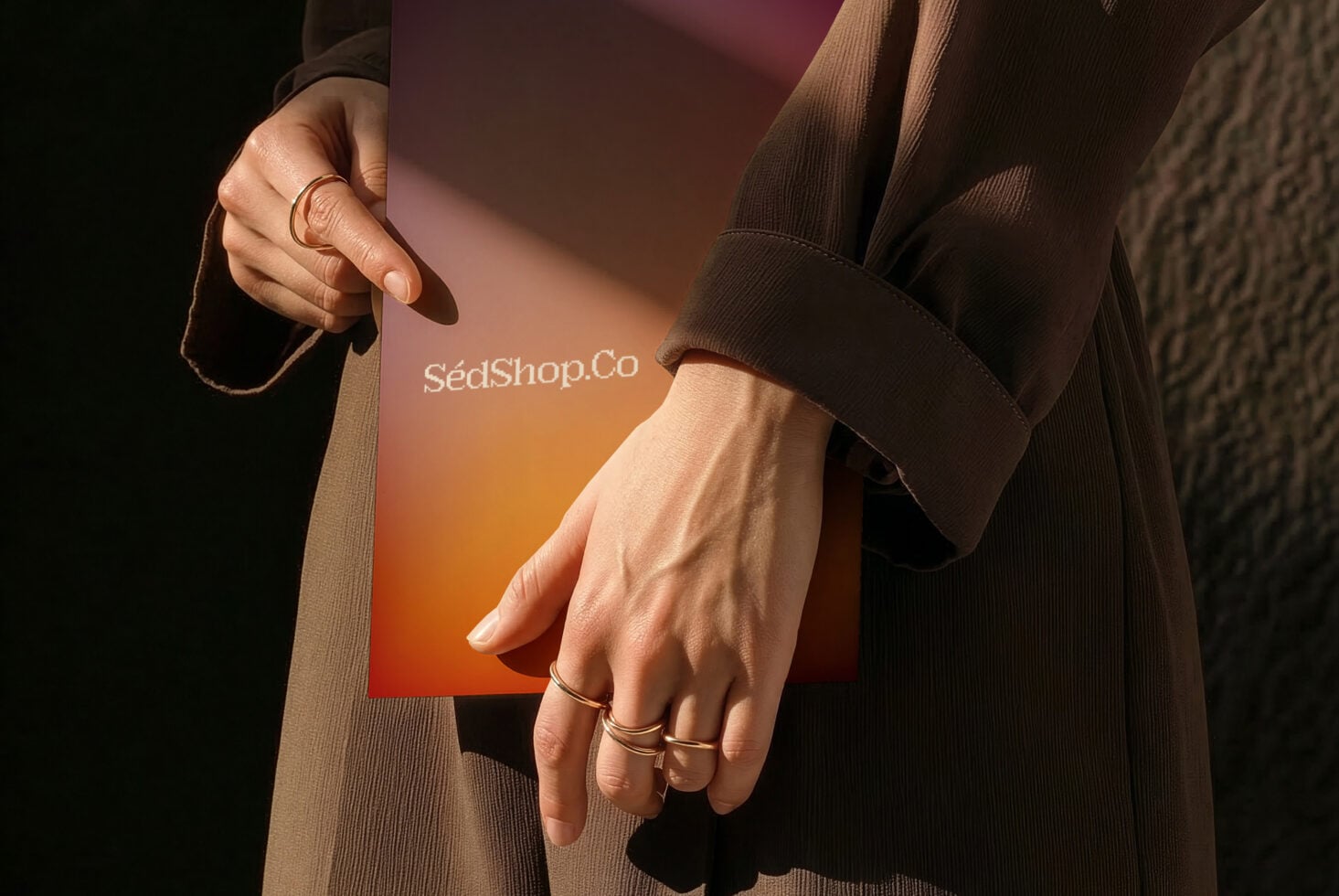 Close-up of hands holding business card with warm gradient, gold rings, brown sweater