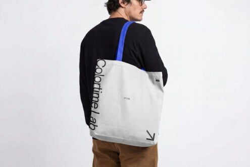 Person wearing cream colored tote bag with blue strap over black shirt