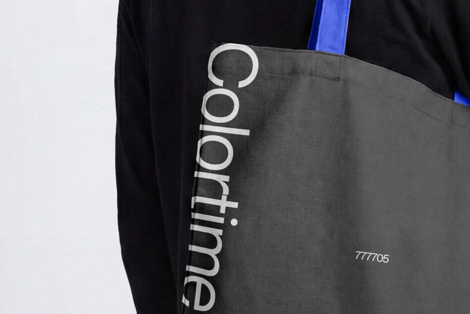 Dark gray tote bag with blue strap slung over person's shoulder from behind