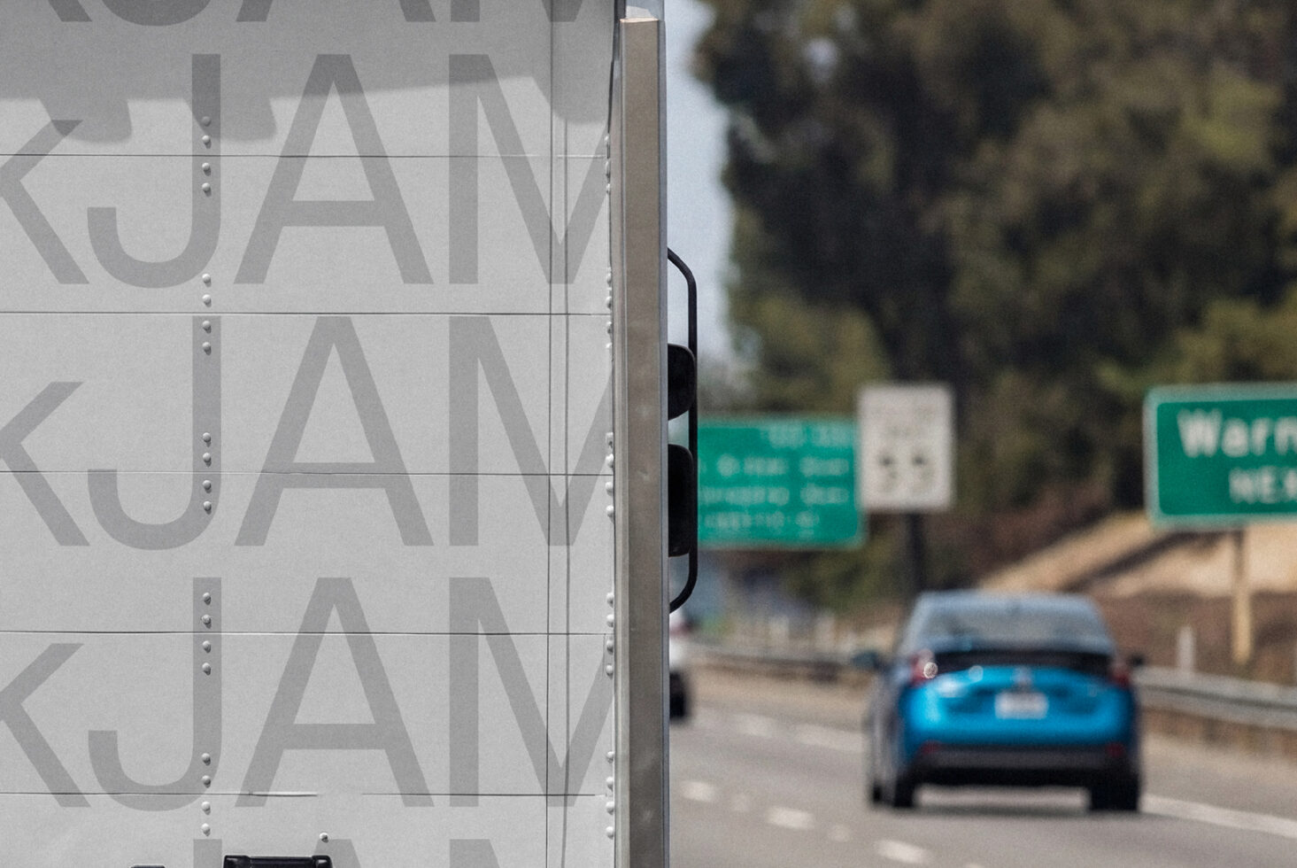 Truck side panel displaying large repeating KUAN letters, blurred highway scene