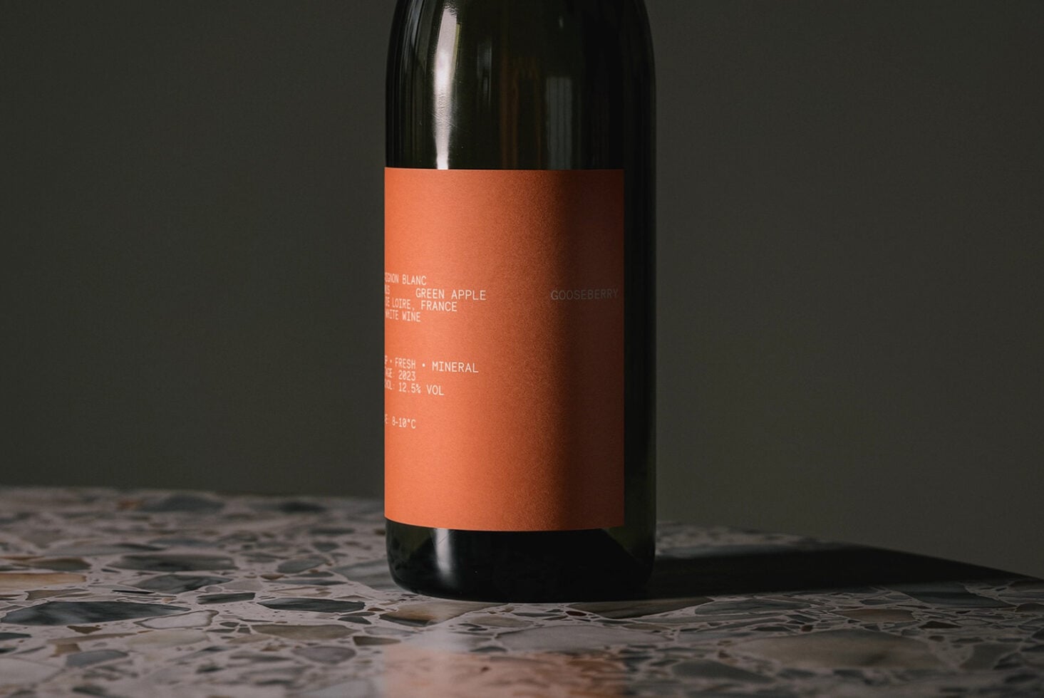 Wine bottle mockup featuring orange label with product details visible on gray backdrop