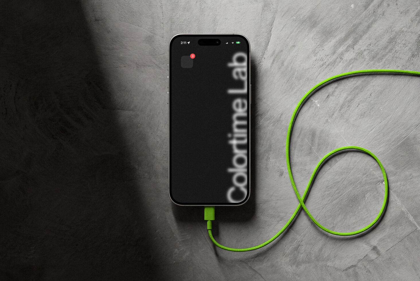 iPhone with dark screen displaying Colortime branding, neon green USB cable on stone surface