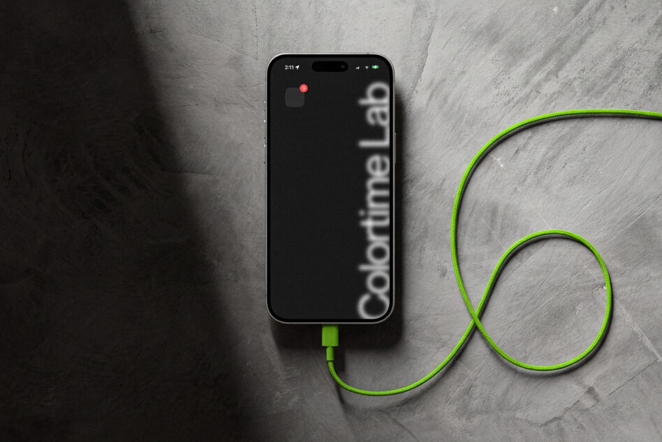 iPhone with dark screen displaying Colortime branding, neon green USB cable on stone surface