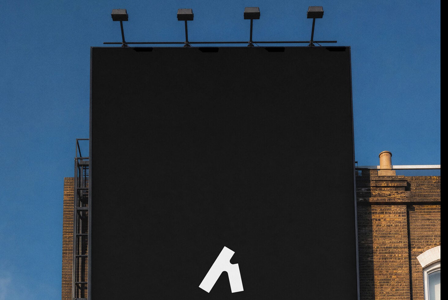 Blank billboard with four lights mounted on top against clear blue sky
