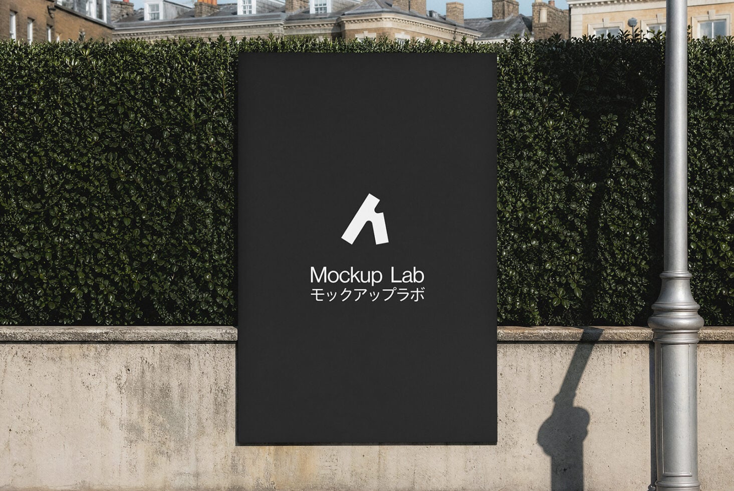 Black billboard mockup mounted on hedged urban wall with London townhouses behind