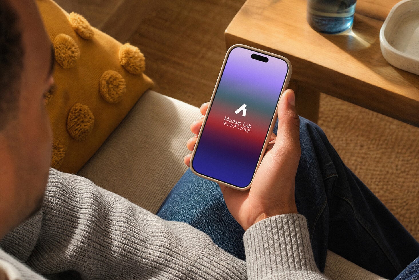 Person holding iPhone with purple gradient screen mockup in cozy home setting with knit cushion