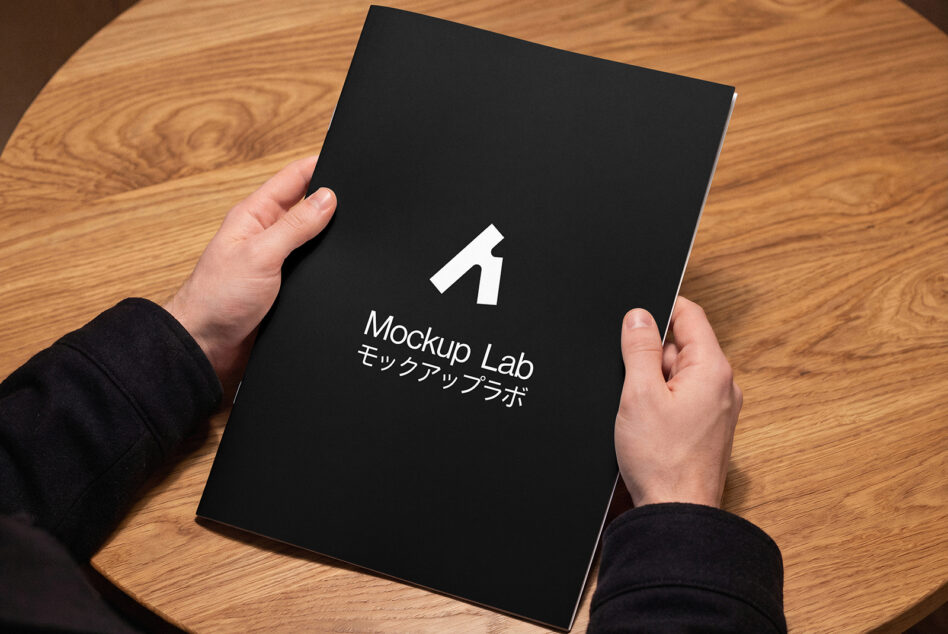 Black book cover held in hands displaying Mockup Lab branding with Japanese characters