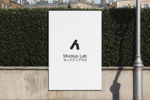 White poster mounted on concrete wall with hedge backdrop, displaying logo with Japanese text