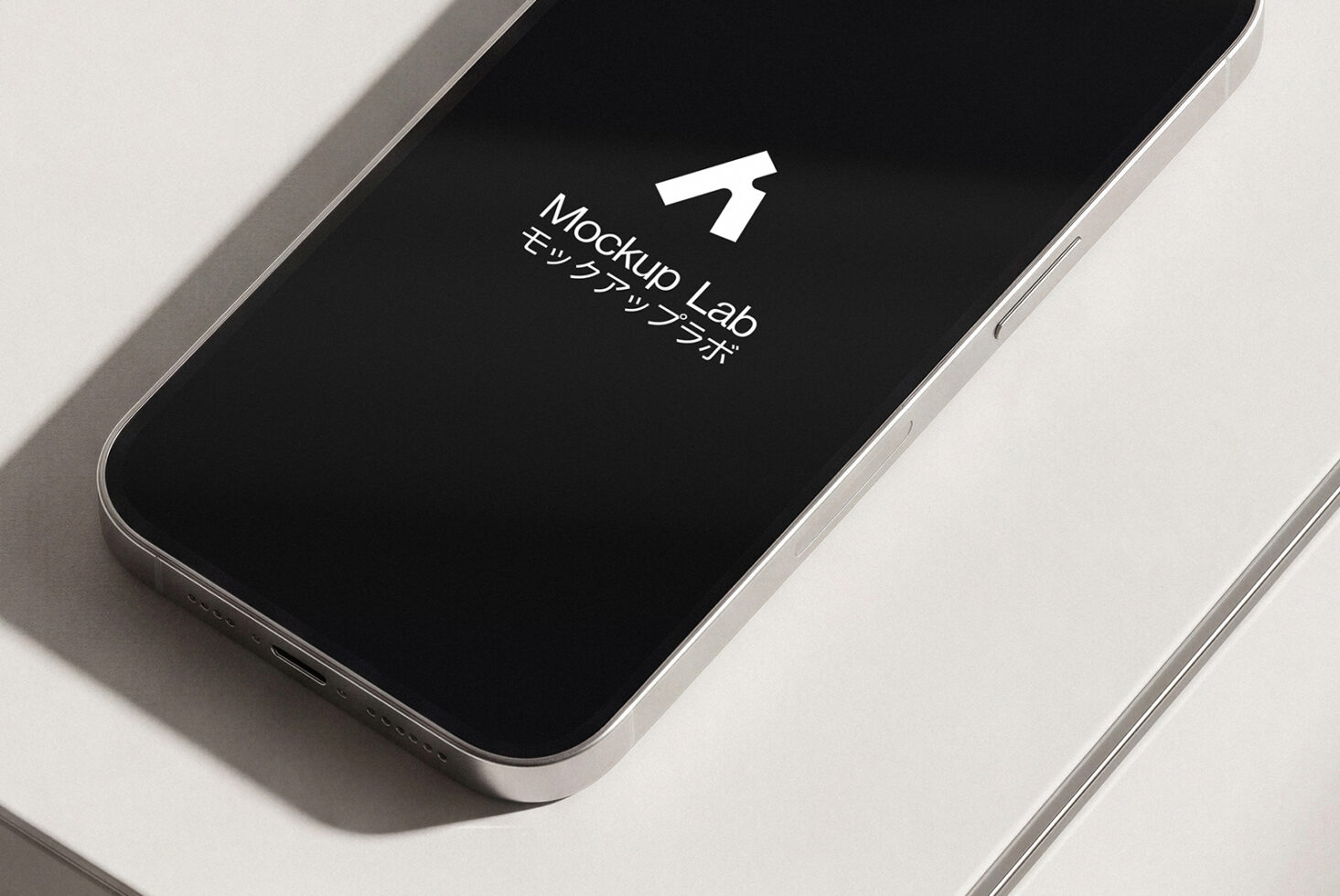 Silver smartphone angled flat lay with black screen displaying white Mockup Lab icon