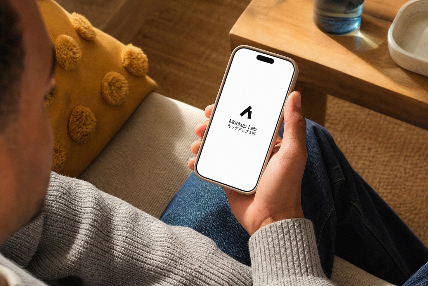Hand holding iPhone 14 Pro with blank screen in cozy home setting with yellow cushion