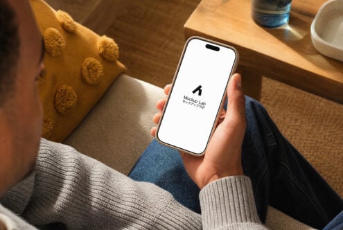Hand holding iPhone 14 Pro with blank screen in cozy home setting with yellow cushion