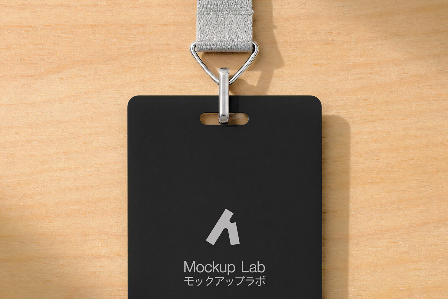 Black ID badge with gray fabric lanyard on wooden surface showing Mockup Lab logo