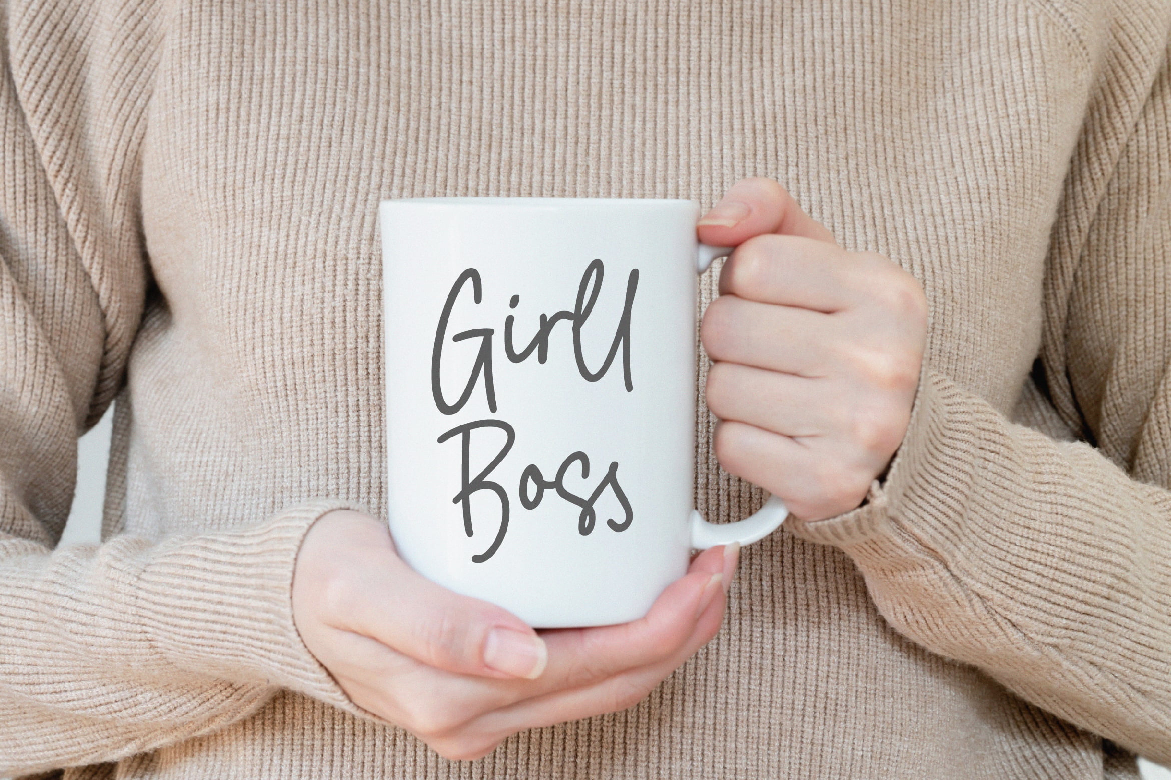 Person holding a white mug with Girl Boss text wearing beige sweater. Mug mockup for designers product display branding inspiration minimalist style.