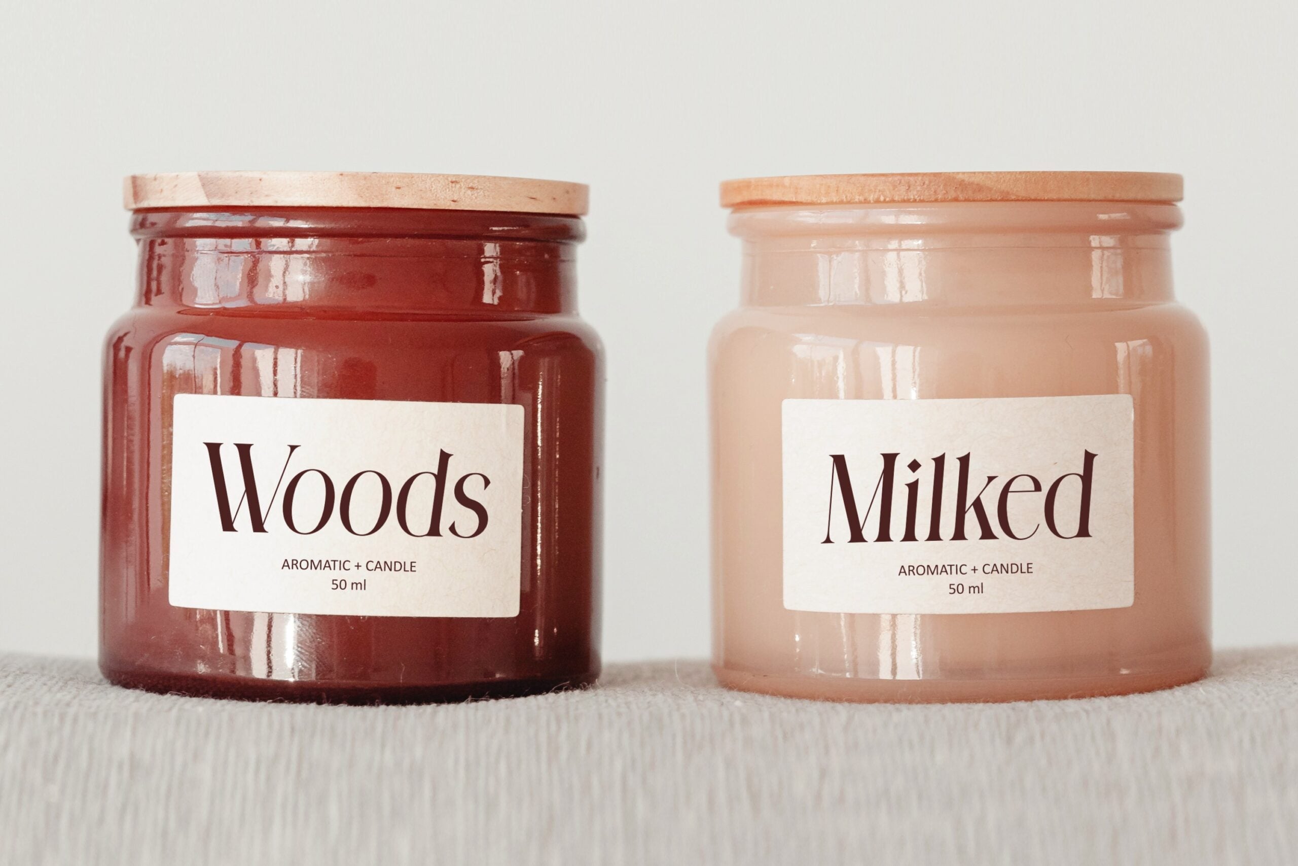 Two glass candle jars side by side, one deep red one pale pink, with minimalist label designs