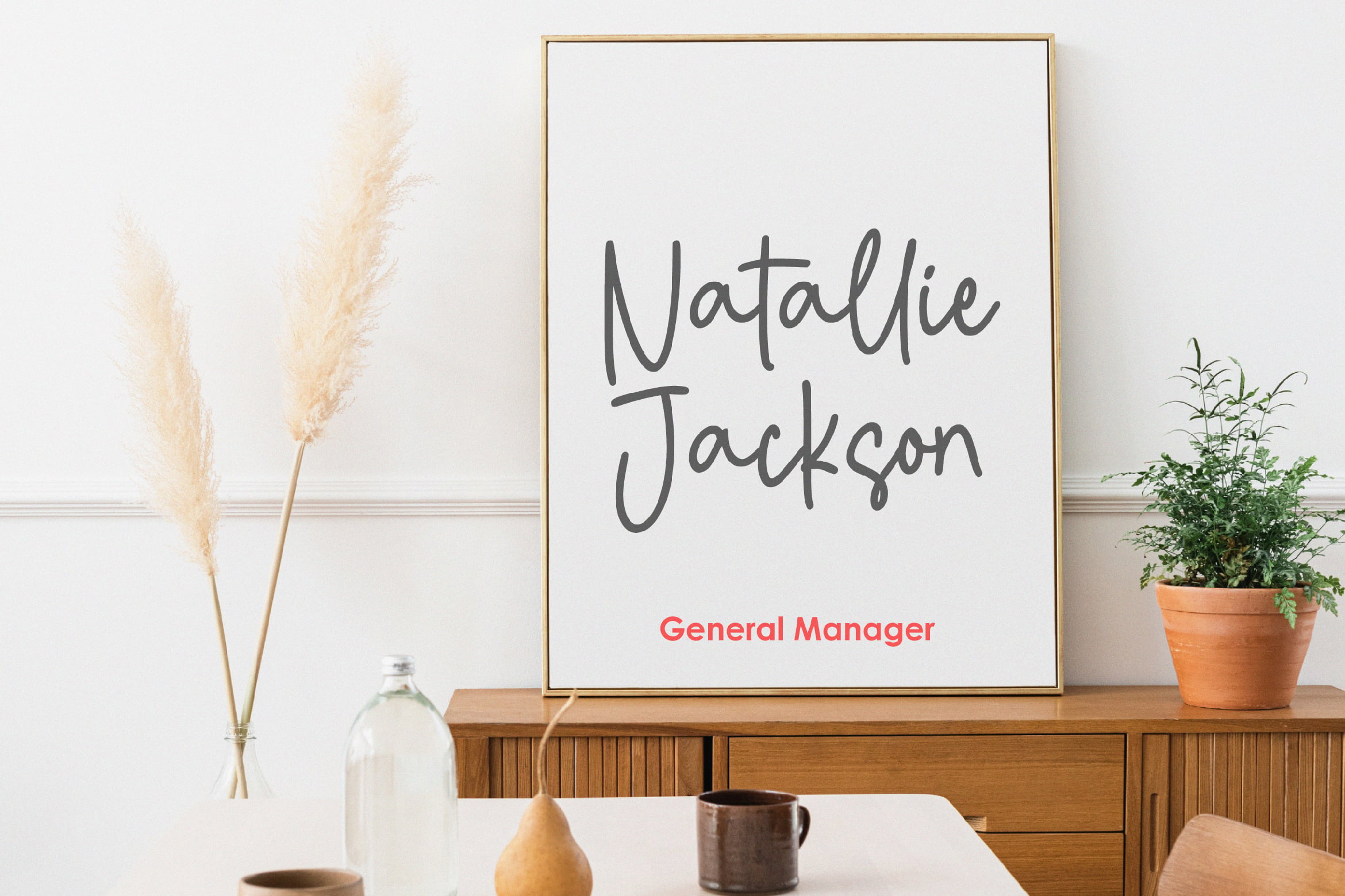 Modern office mockup featuring minimalist design with wooden furniture, decorative pampas grass, and framed text showcasing a handwritten font.