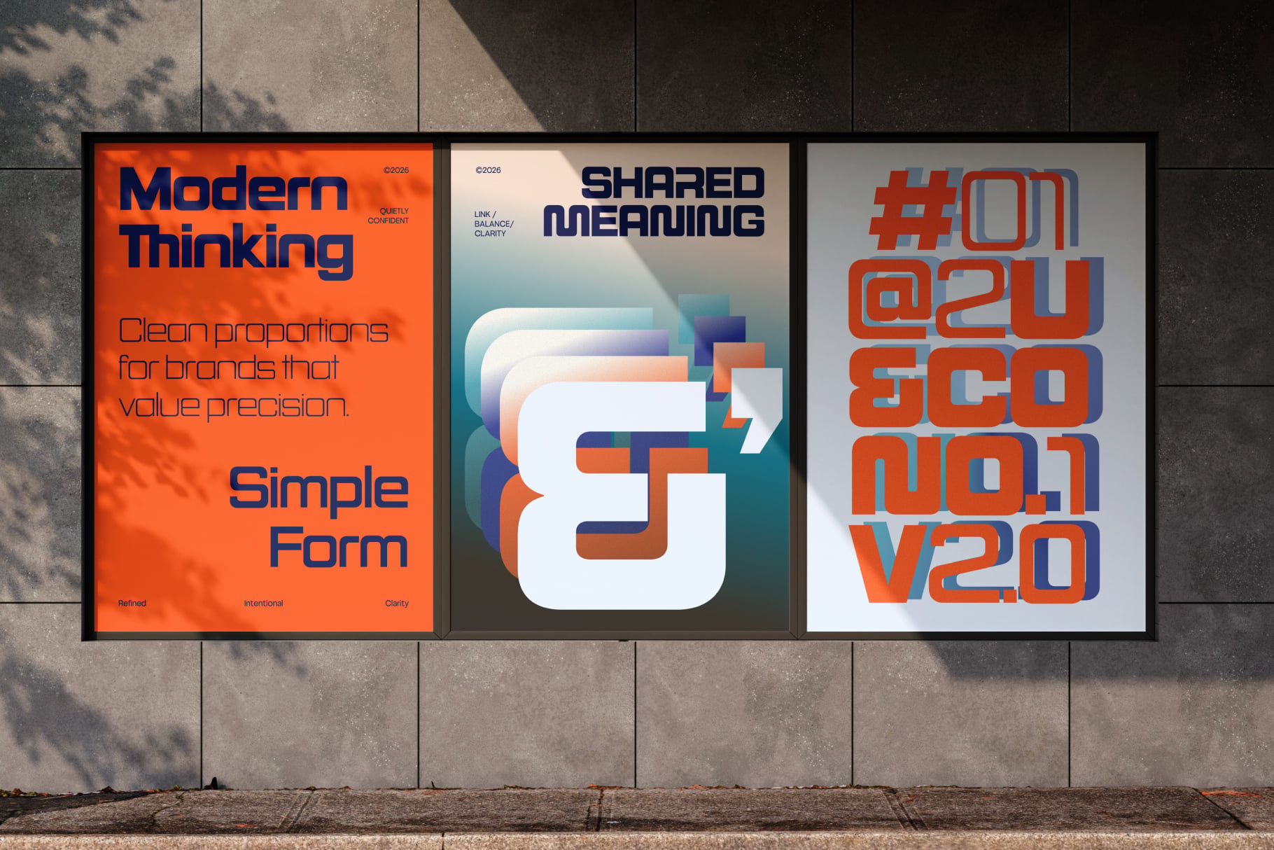 Three framed posters on concrete wall showing modern design work with bold typography in orange, navy, teal colors