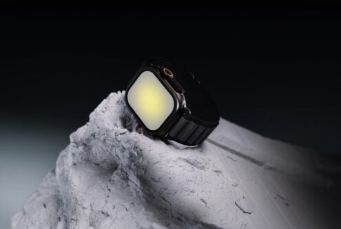 Smartwatch with glowing yellow screen sitting on textured white stone against dark background