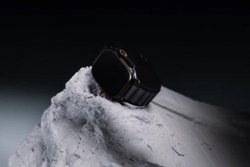 Black smartwatch with gold accents sitting on textured white stone against dark background
