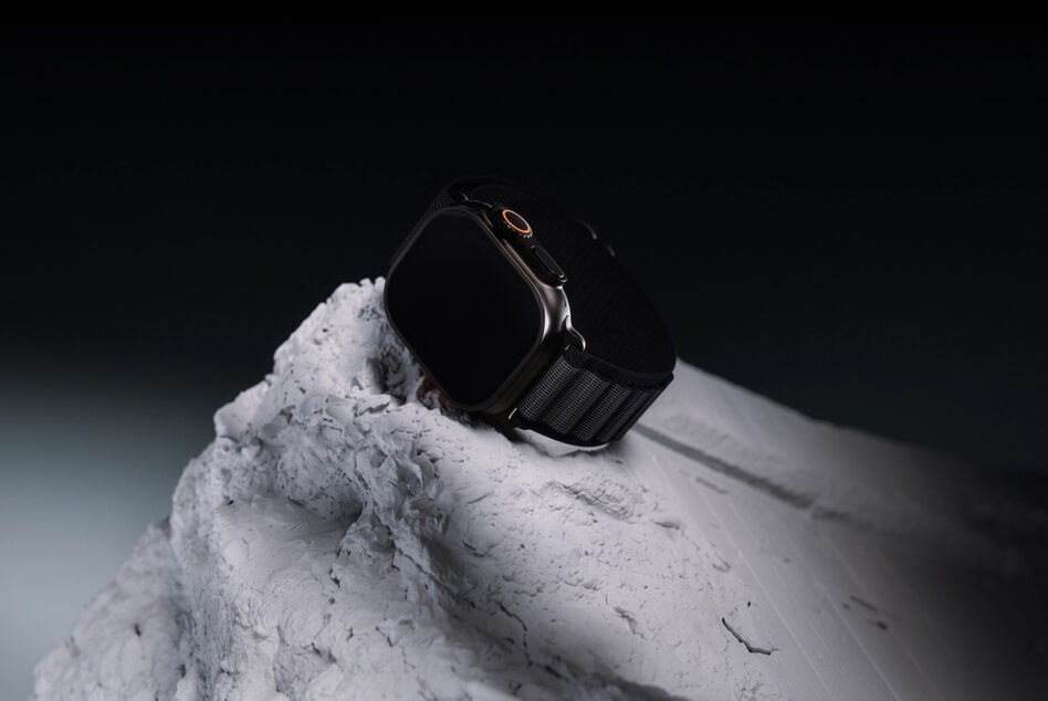 Black smartwatch with gold accents sitting on textured white stone against dark background