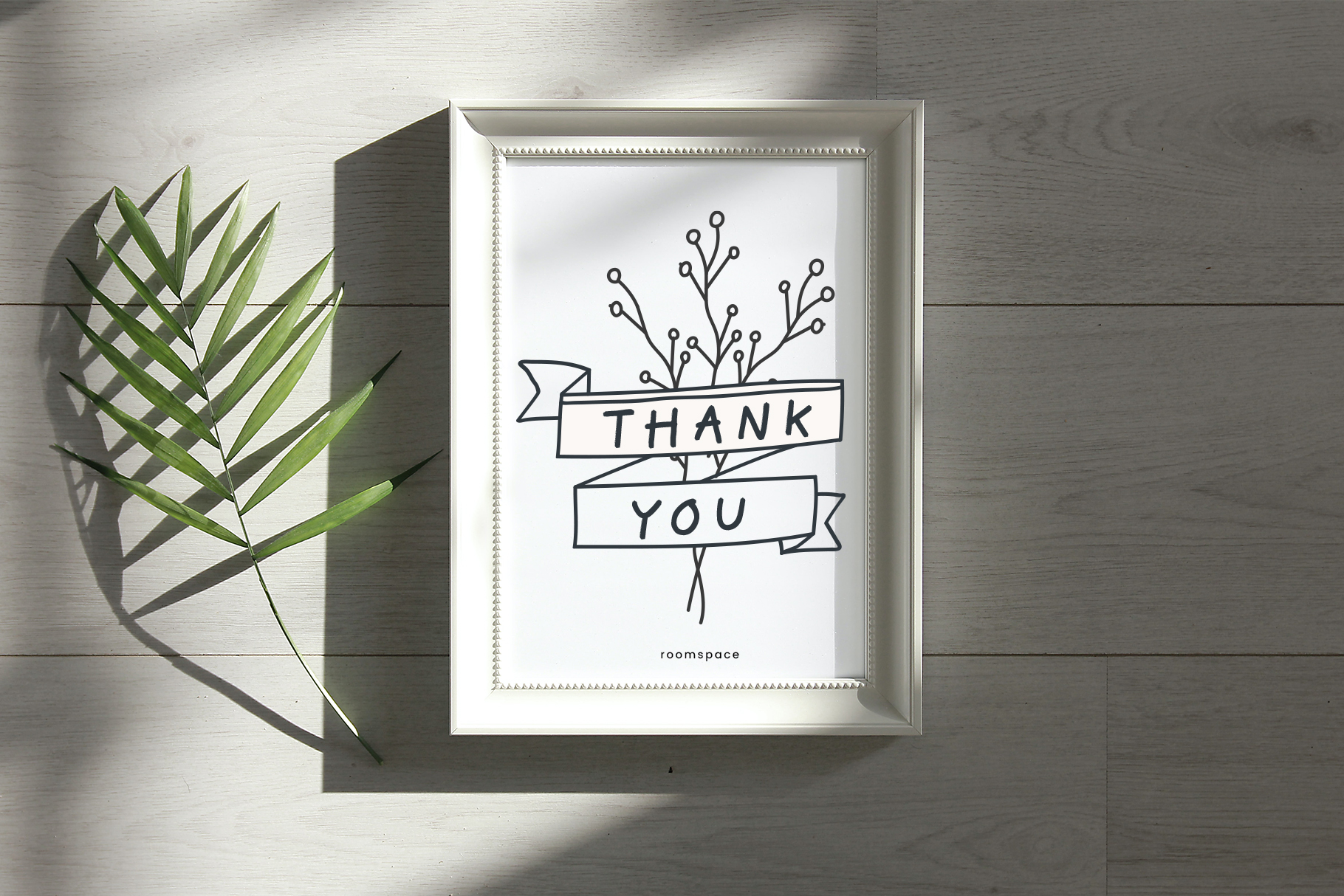 Framed thank you line drawing with plant leaves casting shadows on white wood