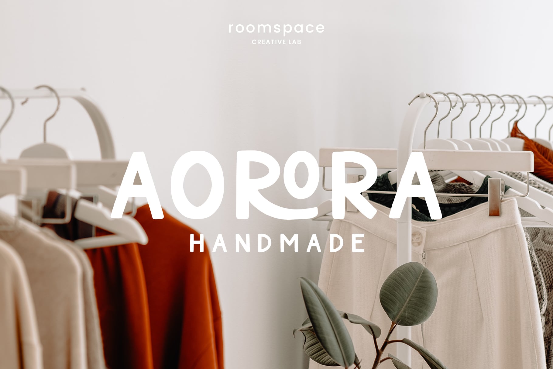 Clothing racks with hangers holding folded garments in cream, rust, showing Aurora Handmade branding overlay